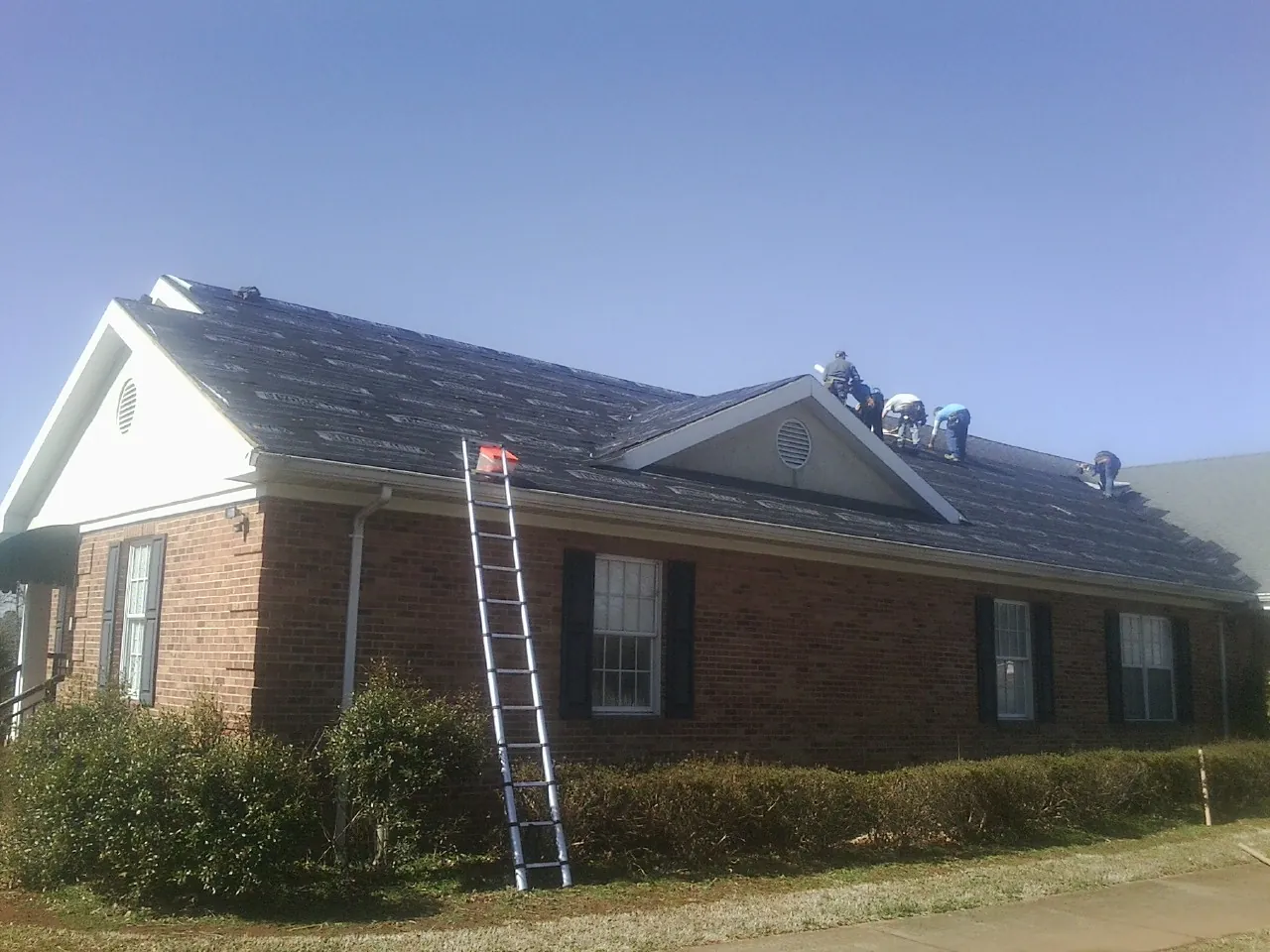 Crew tearing shingles off a brick ranch roof with a ladder set — Emergency Roof Repair work by our crew in San Dimas