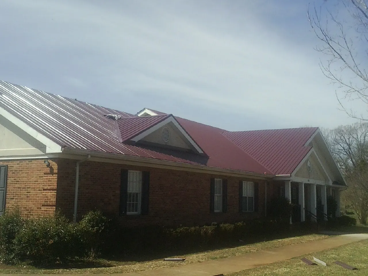 Red metal roof with gabled entries on a long brick building, from a Hail Damage Roof Repair job in San Dimas