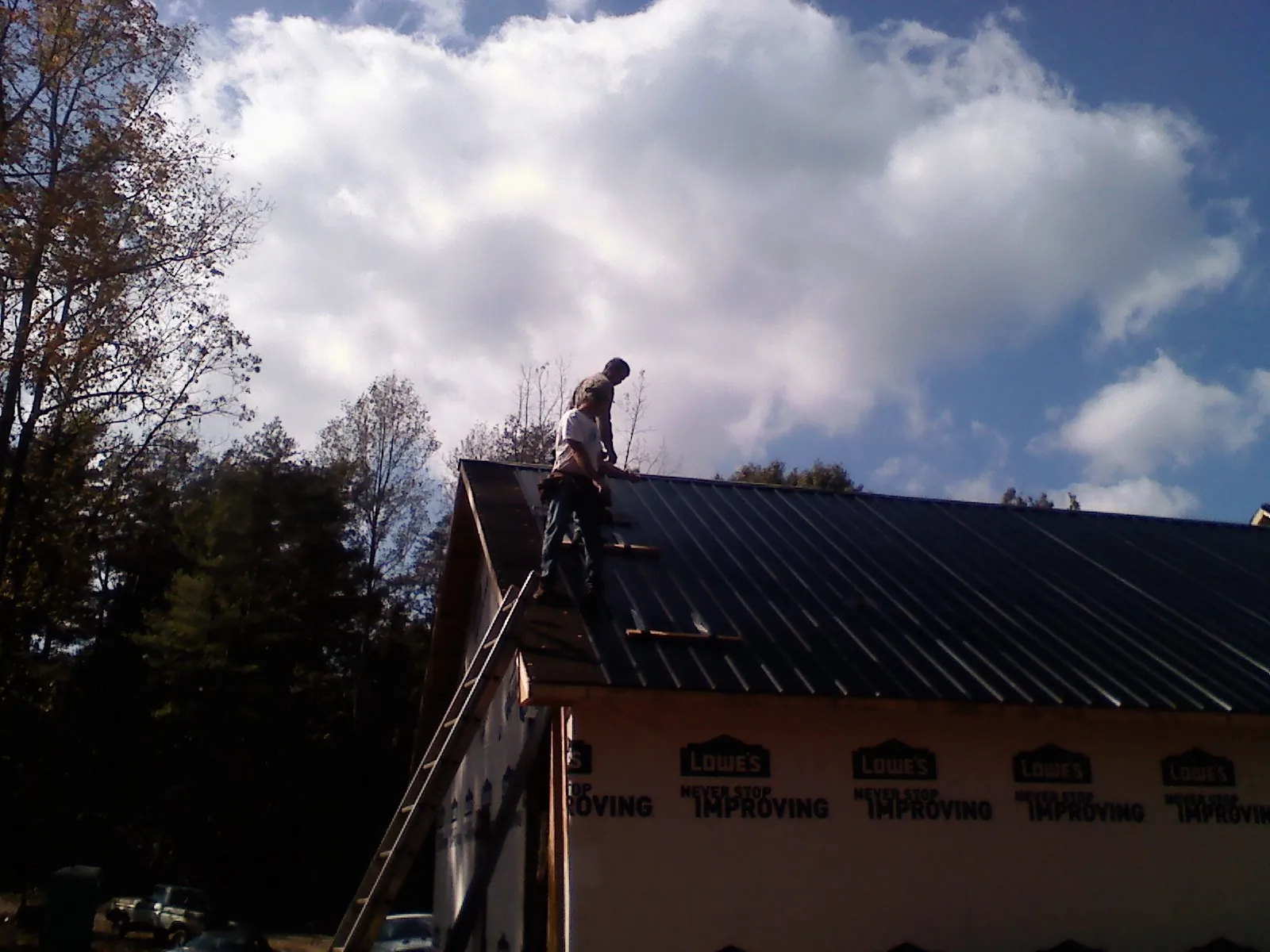 Roofer fastening dark metal panels high against a cloudy sky, from a Roof Inspection job in San Dimas