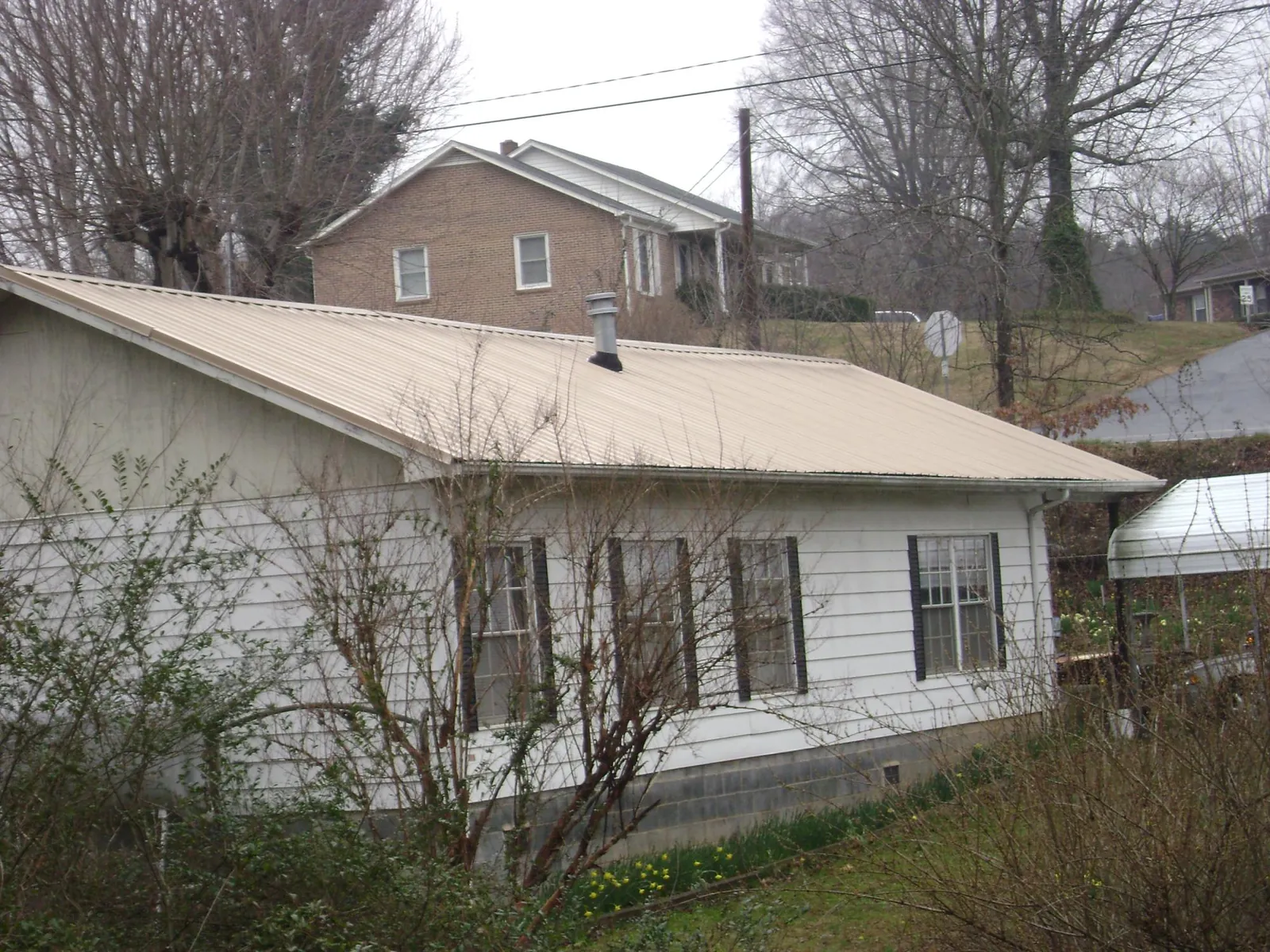 Tan metal roof on a white sided house set into a hillside — Commercial Roofing by Roofing Brothers in San Dimas
